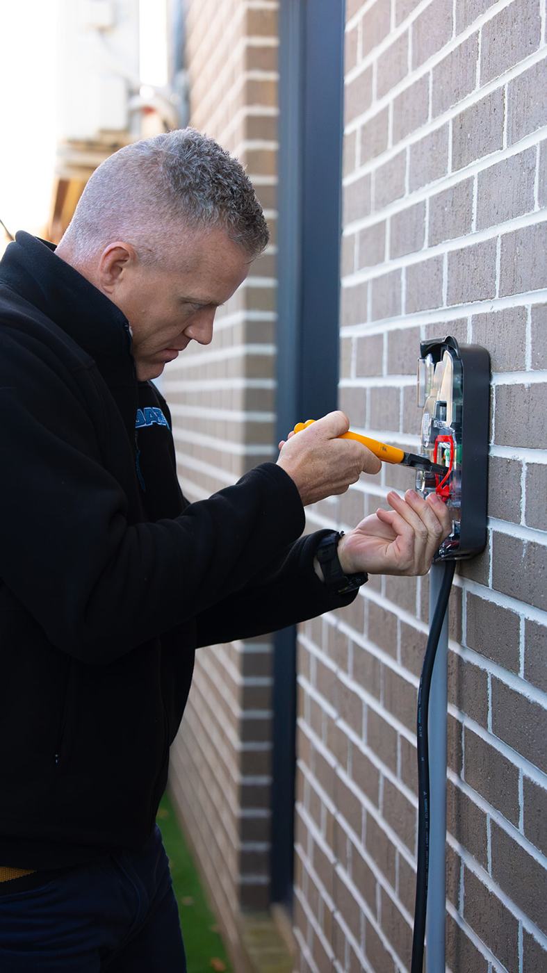 Electrician testing an EV charger on a brick wall