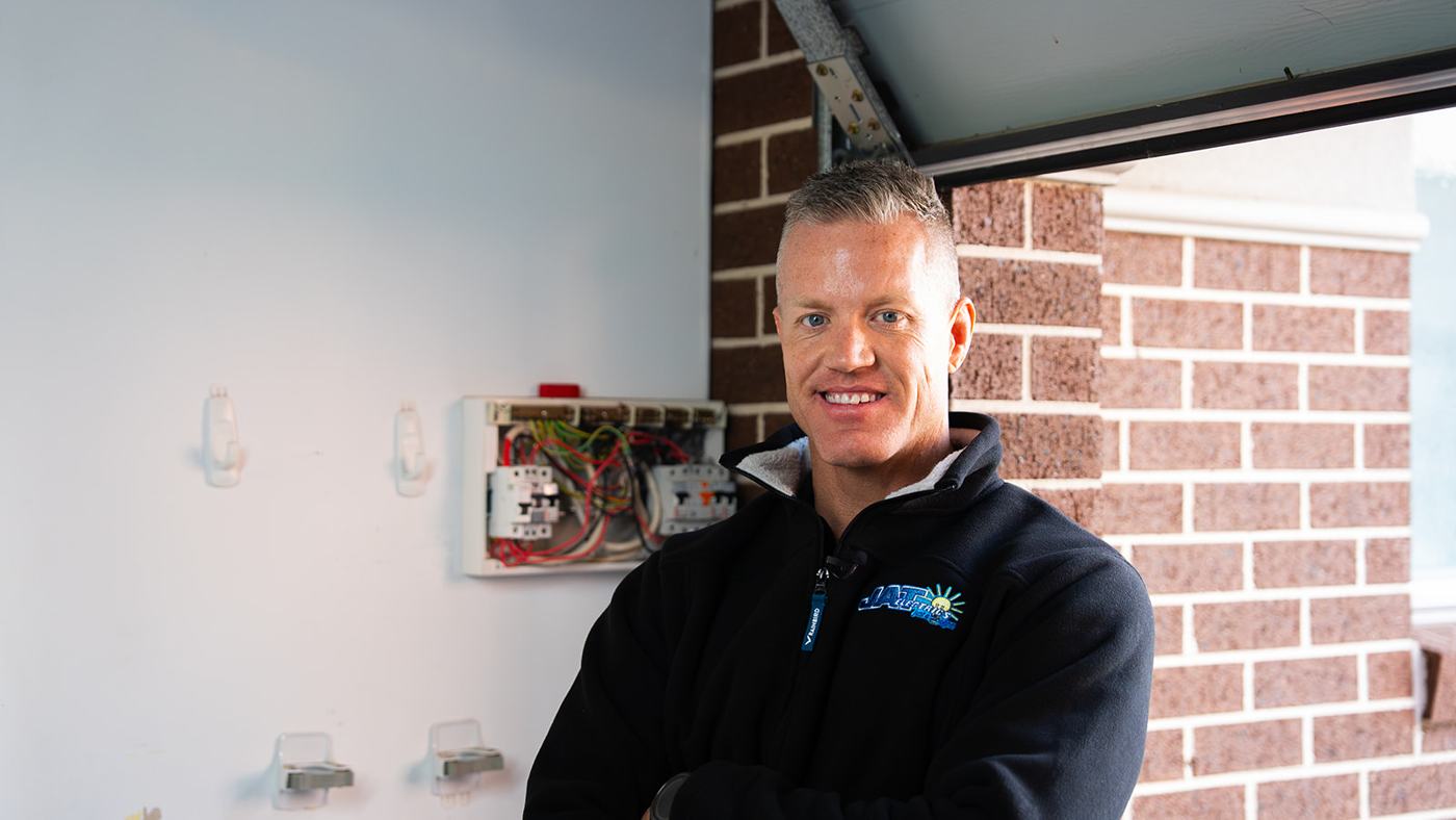 JAT Electrics electrician smiling beside a switchboard