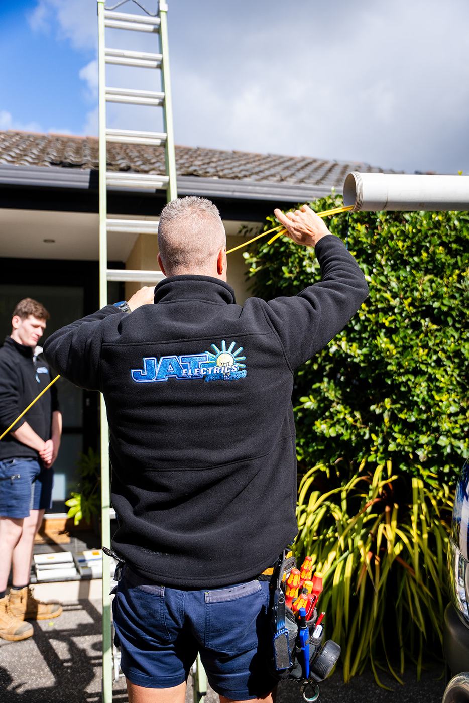 Two electricians working on a roof ladder