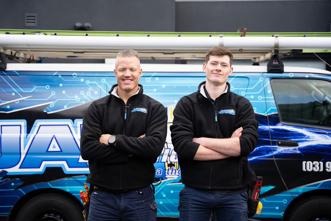 Two JAT Electrics electricians standing arms crossed in front of the JAT van